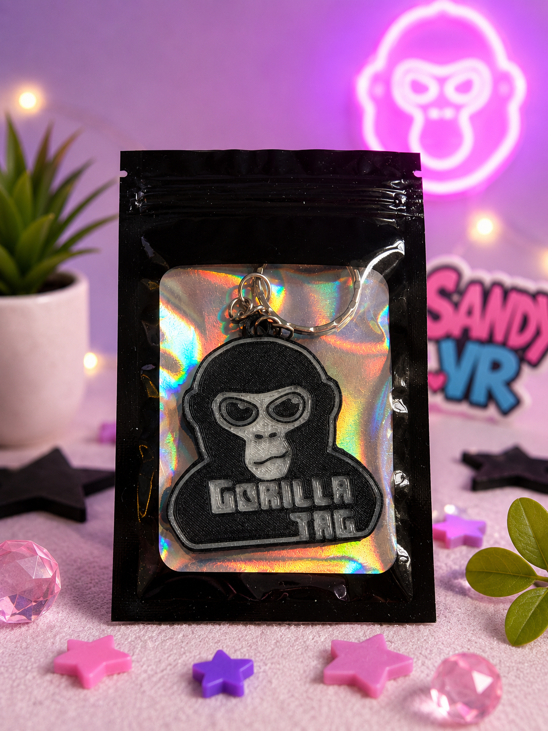 Packaged Gorilla Tag glow-in-the-dark NFC keychain displayed in premium holographic gift packaging with SandyVR branding and decorative gaming-themed background.