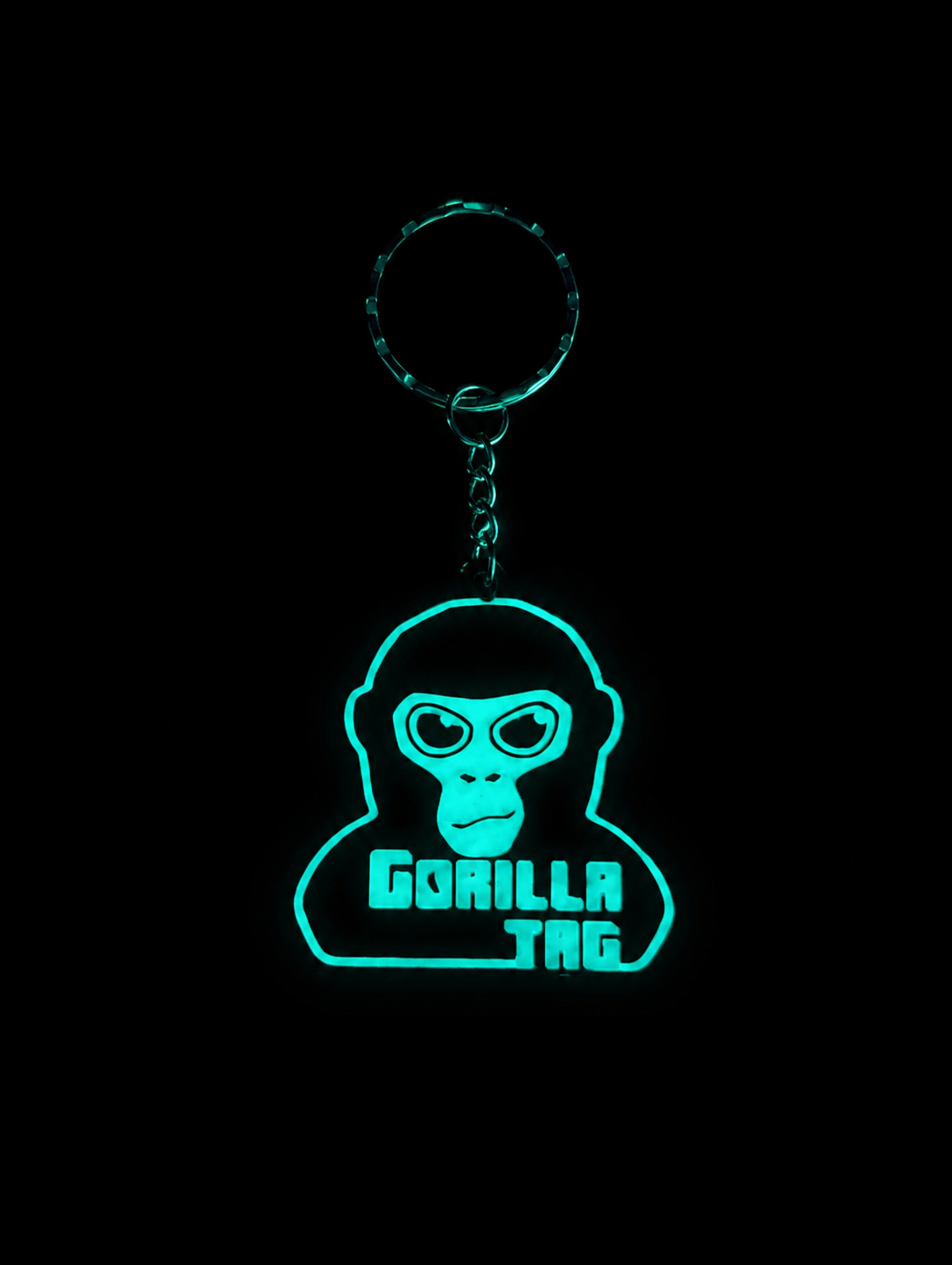 Glow-in-the-dark Gorilla Tag keychain glowing bright green against a black background, showcasing the luminous design and detailed monkey face.